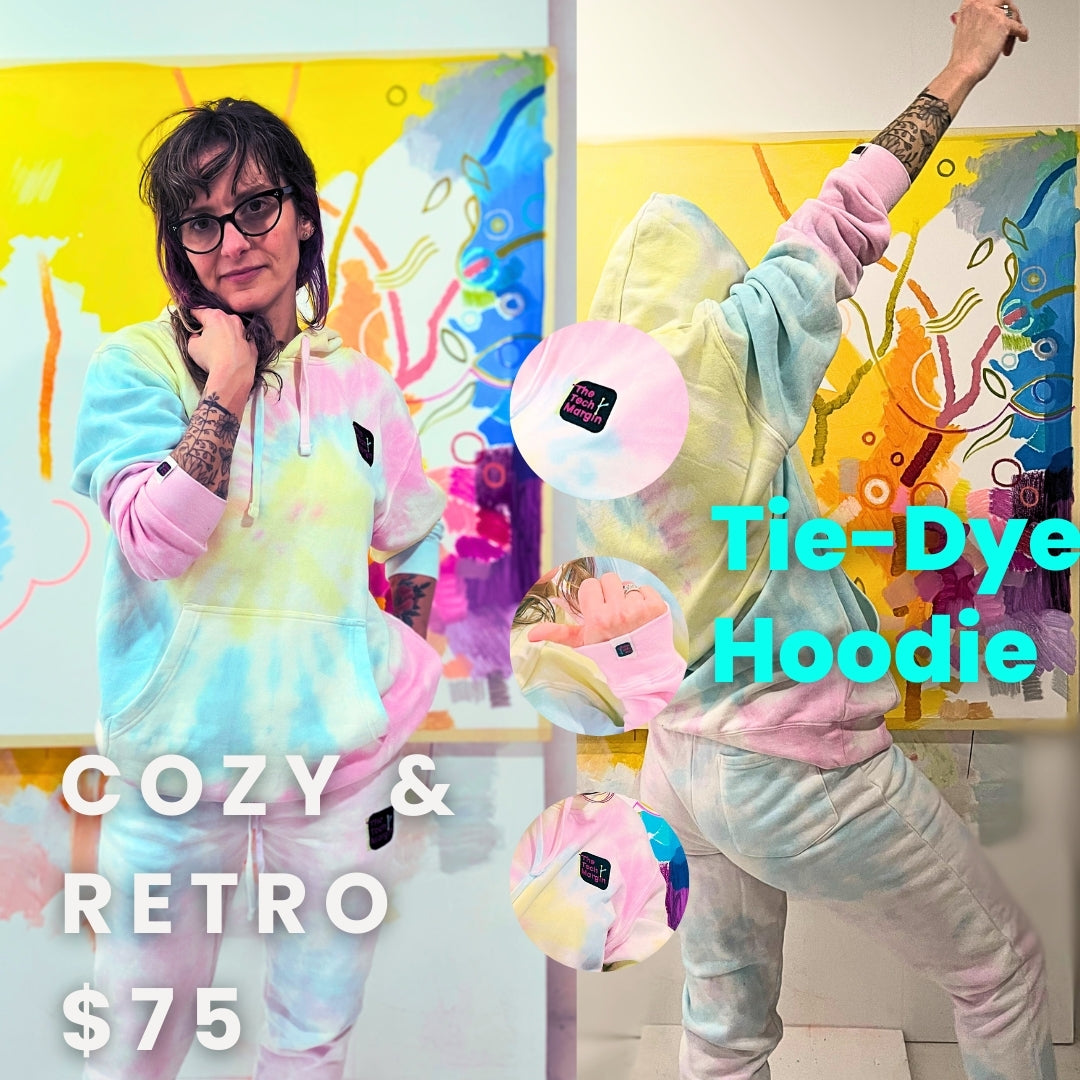 The image presents a striking and colorful portrait, focused on a person wearing a pastel tie-dye hoodie. The hoodie is a blend of soft pink, blue, and yellow hues, creating a dreamy and vibrant aesthetic. The person's pose is casual yet engaging, with one hand partially obscuring their face, drawing attention to the tattooed forearm which features intricate black ink designs.
